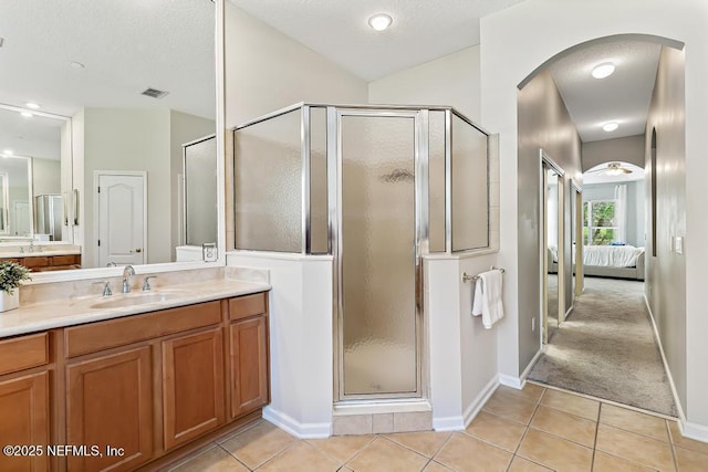 ensuite bathroom with a stall shower, tile patterned flooring, vanity, baseboards, and a textured ceiling