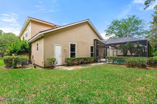 rear view of house featuring stucco siding, a lawn, and a lanai