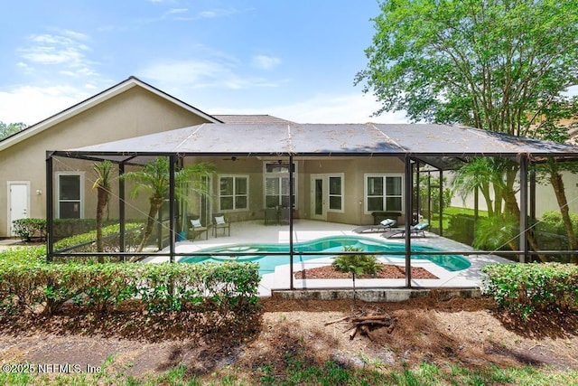 rear view of property featuring stucco siding, a patio area, a ceiling fan, and glass enclosure