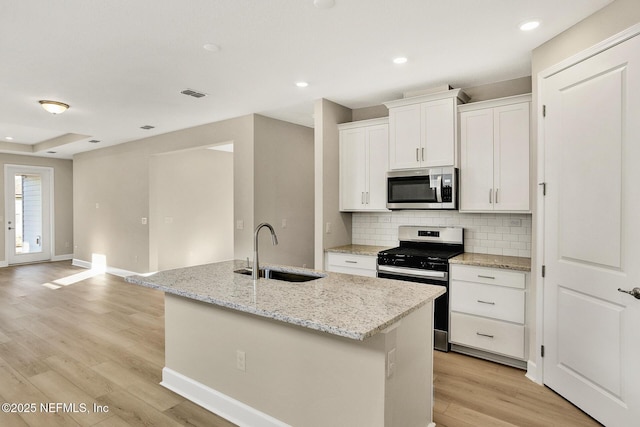 kitchen featuring visible vents, decorative backsplash, a kitchen island with sink, a sink, and stainless steel appliances