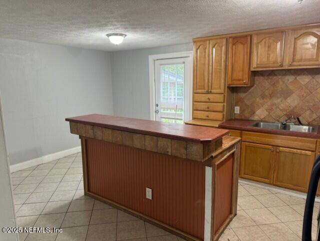 kitchen featuring light tile patterned flooring, a center island, a sink, and tasteful backsplash