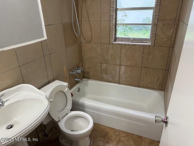 bathroom with a sink, washtub / shower combination, toilet, and tile walls