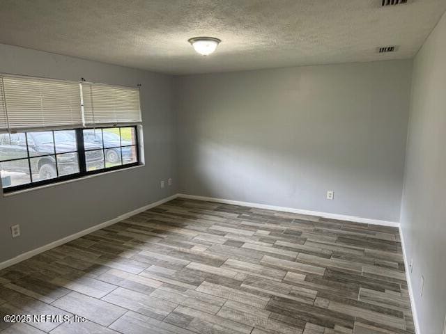 unfurnished room with baseboards, a textured ceiling, visible vents, and wood finished floors