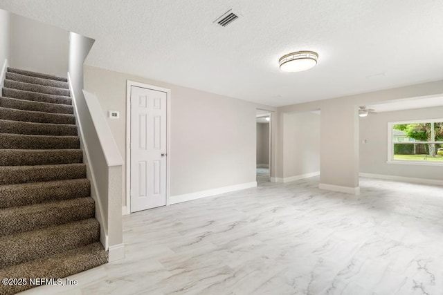 unfurnished living room featuring a textured ceiling, visible vents, baseboards, marble finish floor, and stairs