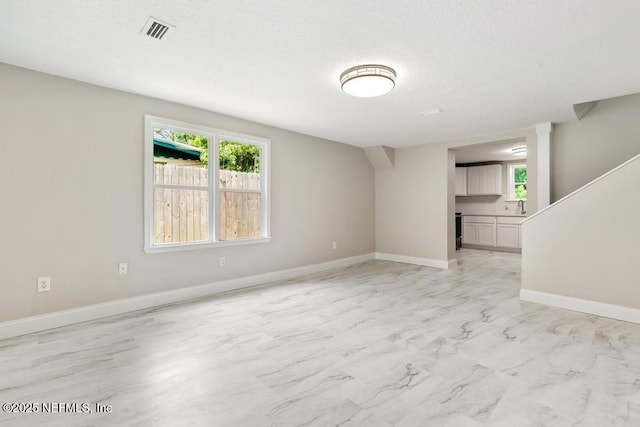 unfurnished living room with baseboards, a sink, visible vents, and a healthy amount of sunlight