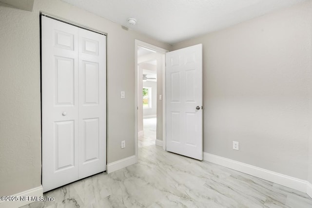 unfurnished bedroom with baseboards, marble finish floor, and a closet