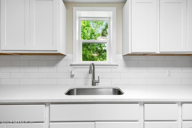 kitchen featuring light stone counters, a sink, decorative backsplash, and white cabinets