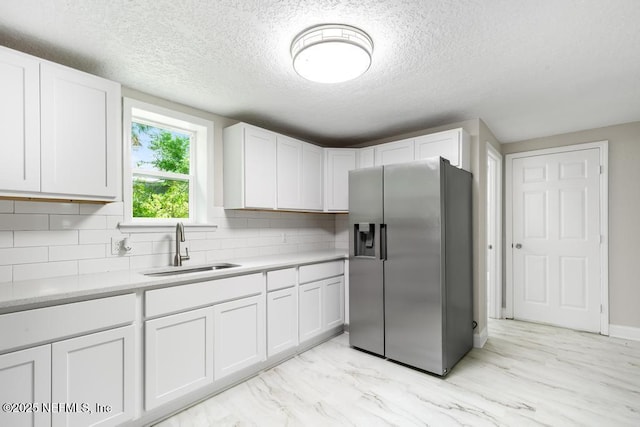 kitchen featuring stainless steel fridge, a textured ceiling, a sink, and light countertops