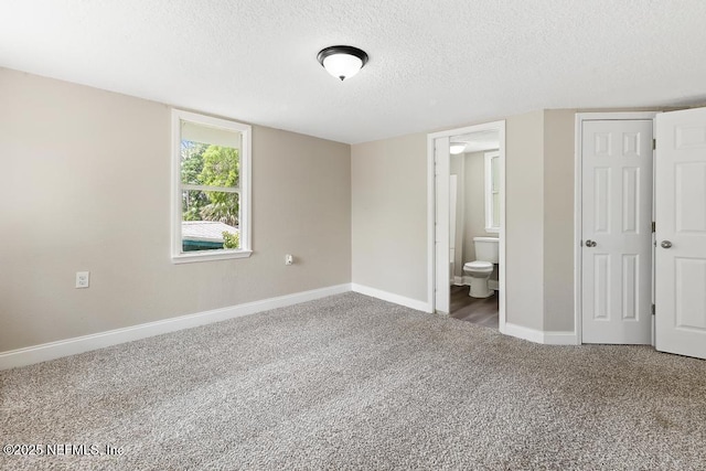 unfurnished bedroom with carpet flooring, a textured ceiling, baseboards, and ensuite bath