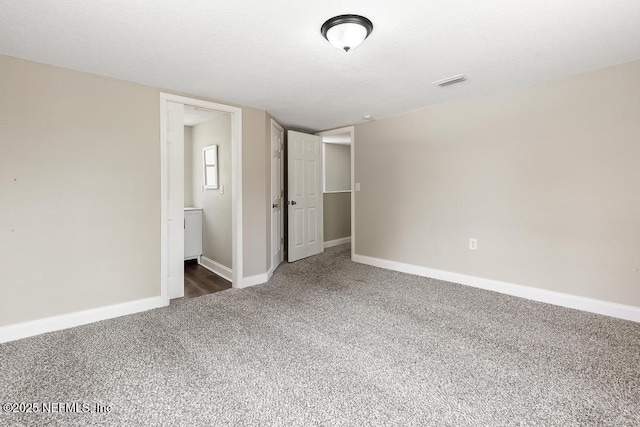 unfurnished bedroom featuring carpet floors, baseboards, ensuite bath, and visible vents