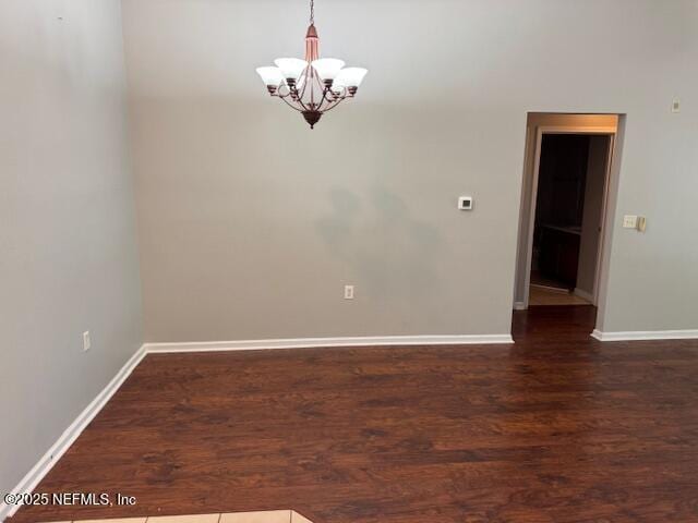unfurnished room with dark wood-style flooring, baseboards, and an inviting chandelier