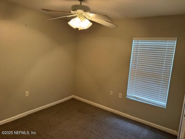 empty room with ceiling fan, baseboards, and dark colored carpet