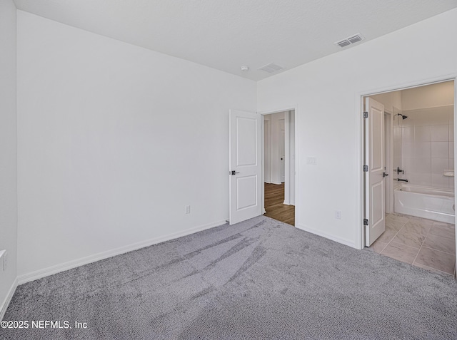 unfurnished bedroom featuring baseboards, ensuite bath, carpet floors, and visible vents