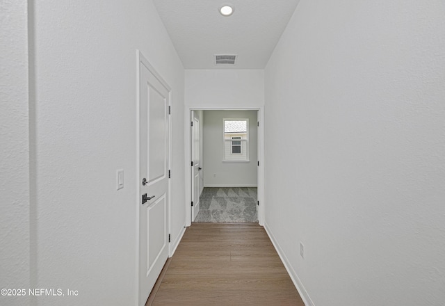 corridor with visible vents, baseboards, and wood finished floors