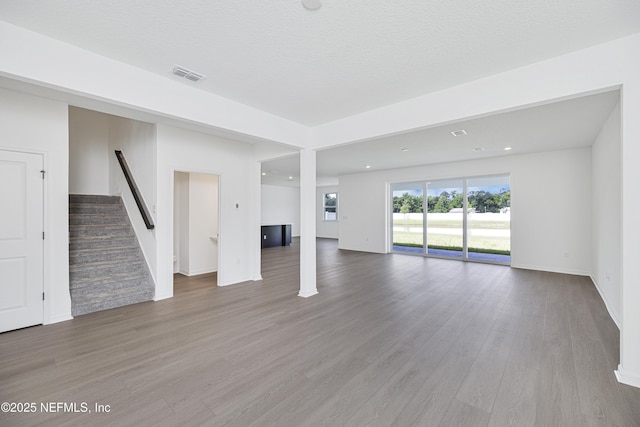unfurnished living room featuring stairway, baseboards, wood finished floors, and visible vents