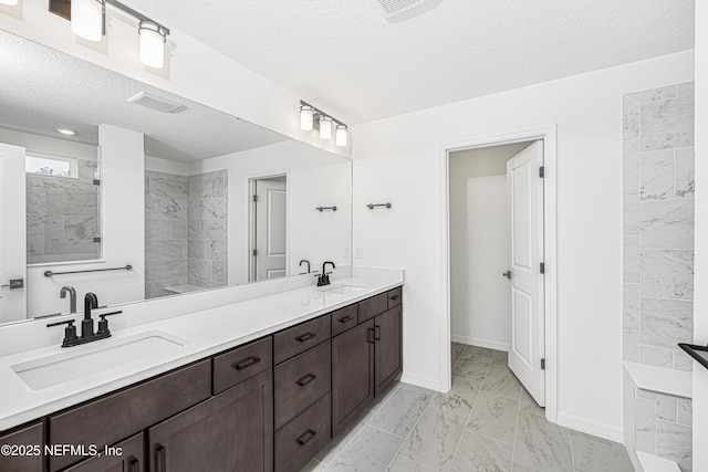 full bathroom with double vanity, a textured ceiling, a sink, and marble finish floor