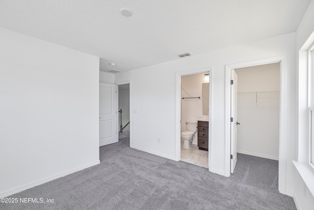 unfurnished bedroom featuring carpet floors, visible vents, a closet, baseboards, and a walk in closet