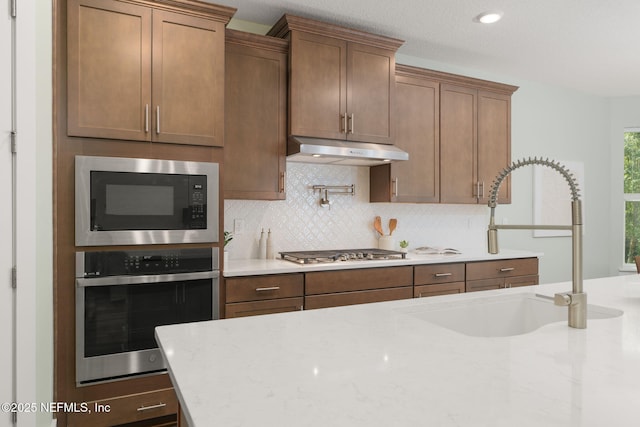55 Rainbow Trout Ln, Ponte Vedra, FL 32081 - kitchen with appliances with stainless steel finishes, under cabinet range hood, a sink, decorative backsplash, and light stone counters
