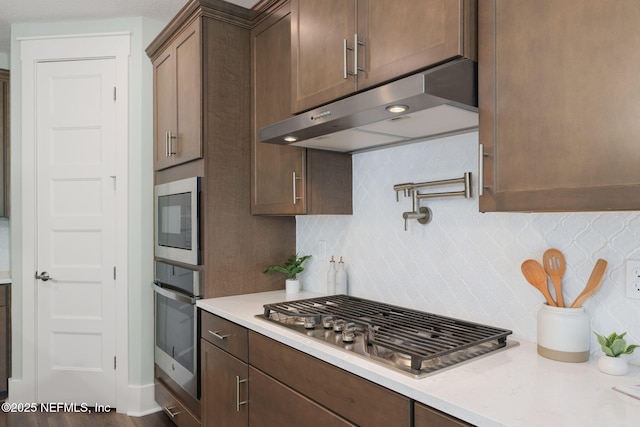 55 Rainbow Trout Ln, Ponte Vedra, FL 32081 - kitchen with under cabinet range hood, appliances with stainless steel finishes, decorative backsplash, and dark brown cabinets