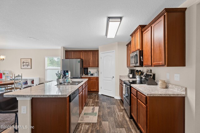 kitchen with appliances with stainless steel finishes, a sink, light countertops, dark wood-type flooring, and a center island with sink