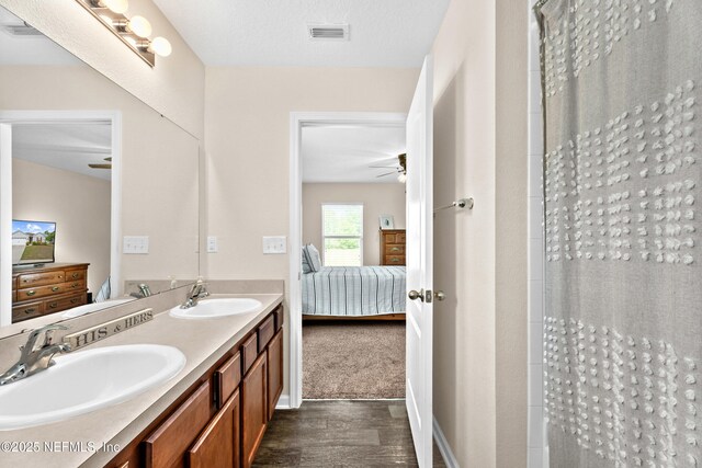 ensuite bathroom with visible vents, a sink, connected bathroom, and wood finished floors