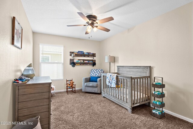 bedroom featuring carpet floors, a nursery area, baseboards, and a ceiling fan
