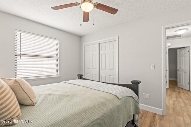7372 Secret Woods Dr, Jacksonville, FL 32216 - bedroom featuring a closet, light wood-type flooring, baseboards, ceiling fan, and a textured ceiling