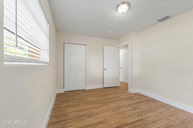 unfurnished bedroom featuring visible vents, baseboards, wood finished floors, and a closet