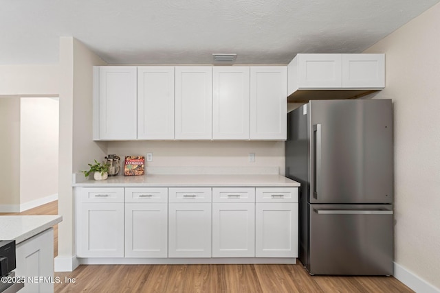 kitchen with white cabinets, light countertops, freestanding refrigerator, light wood-type flooring, and visible vents
