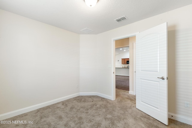 spare room featuring light colored carpet, baseboards, and visible vents