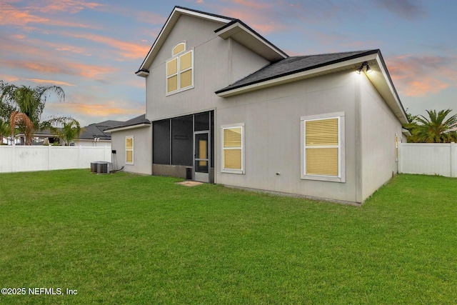 back of house at dusk featuring a sunroom, a fenced backyard, central air condition unit, and a yard