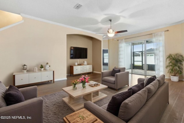 living area featuring crown molding, a ceiling fan, arched walkways, and wood finished floors