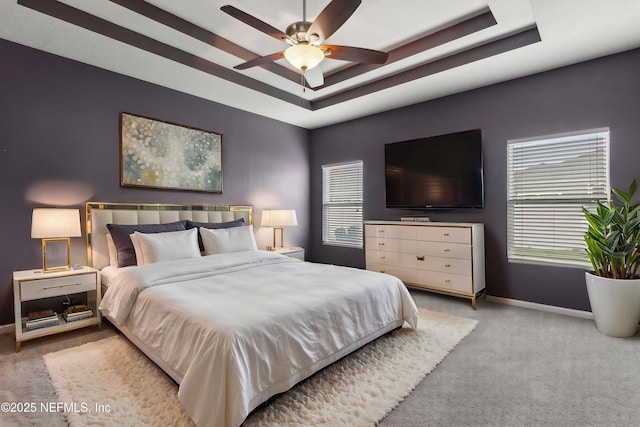 carpeted bedroom with a ceiling fan, a tray ceiling, and baseboards