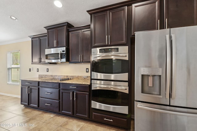 kitchen featuring dark brown cabinetry, light tile patterned flooring, a textured ceiling, light stone counters, and appliances with stainless steel finishes