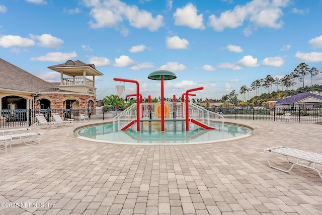 view of play area with fence, a patio, a community pool, and a water play area