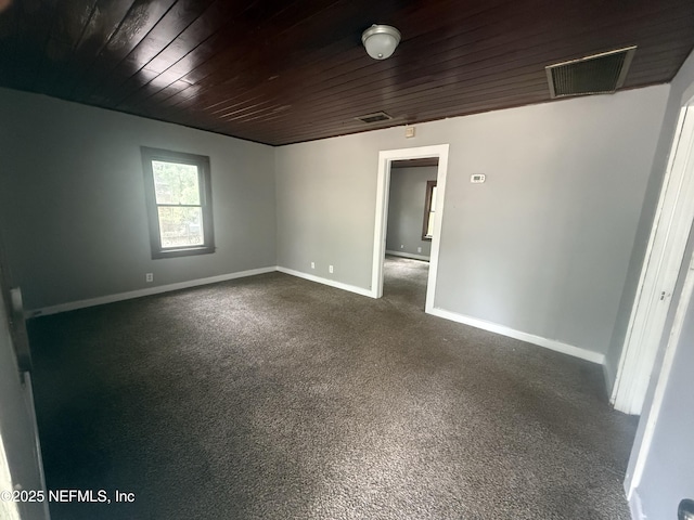 empty room with wood ceiling, baseboards, dark carpet, and visible vents