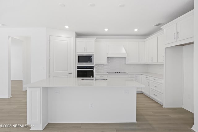 2413 Glade Ln, Green Cove Springs, FL 32043 - kitchen with black appliances, custom range hood, a center island with sink, light wood finished floors, and recessed lighting