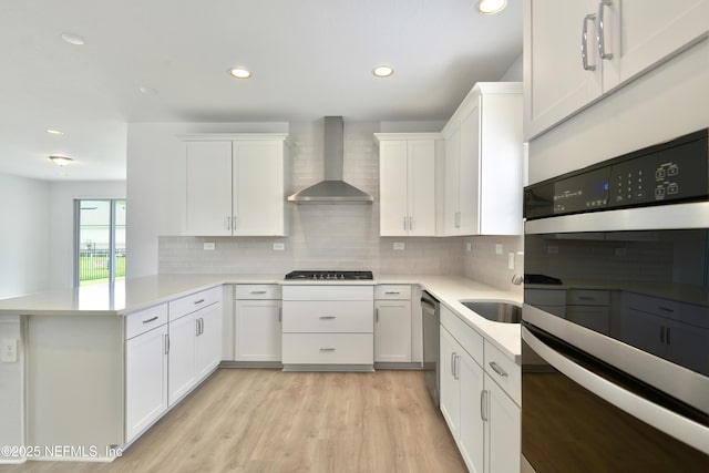 kitchen featuring wall chimney exhaust hood, a peninsula, white cabinetry, stainless steel appliances, and backsplash