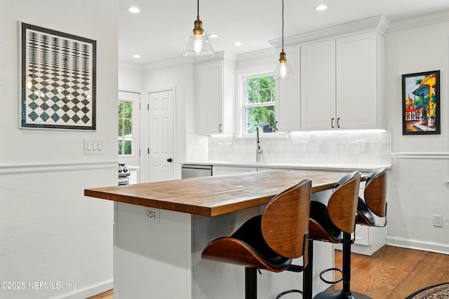 kitchen with a sink, light wood finished floors, white cabinetry, backsplash, and butcher block counters