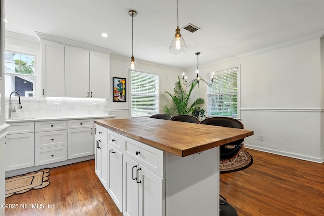 kitchen with crown molding, butcher block counters, wood finished floors, white cabinetry, and a sink