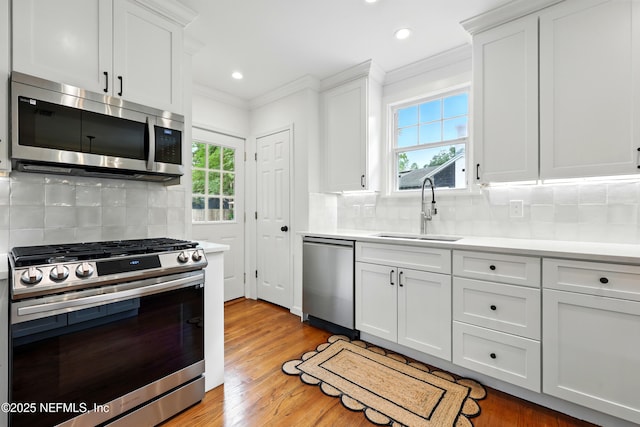 kitchen with a sink, light countertops, ornamental molding, and stainless steel appliances