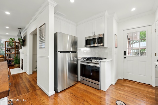 kitchen featuring appliances with stainless steel finishes, plenty of natural light, ornamental molding, and light wood-style flooring