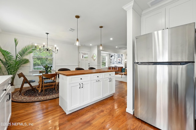 kitchen with wooden counters, visible vents, white cabinets, freestanding refrigerator, and a notable chandelier