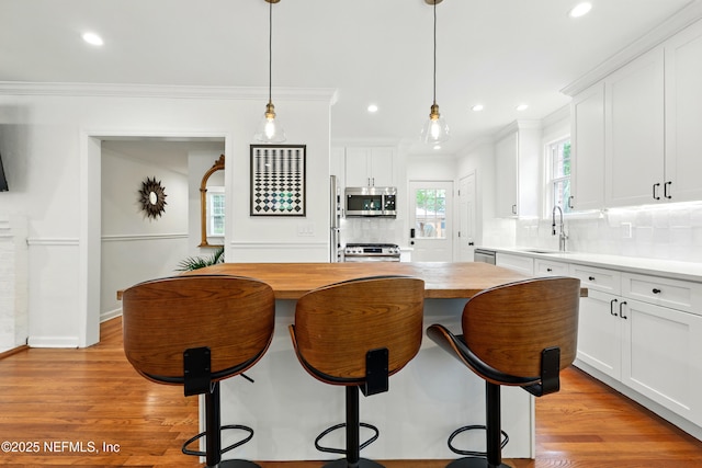 kitchen with a kitchen breakfast bar, backsplash, appliances with stainless steel finishes, a sink, and butcher block countertops