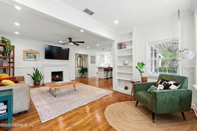 living room with ornamental molding, recessed lighting, wood finished floors, and visible vents
