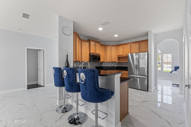 132 Summerhill Cir, Saint Augustine, FL 32086 - kitchen with freestanding refrigerator, dark countertops, light marble finish flooring, a kitchen breakfast bar, and arched walkways
