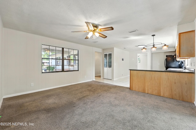 unfurnished living room with ceiling fan, visible vents, light colored carpet, a sink, and baseboards