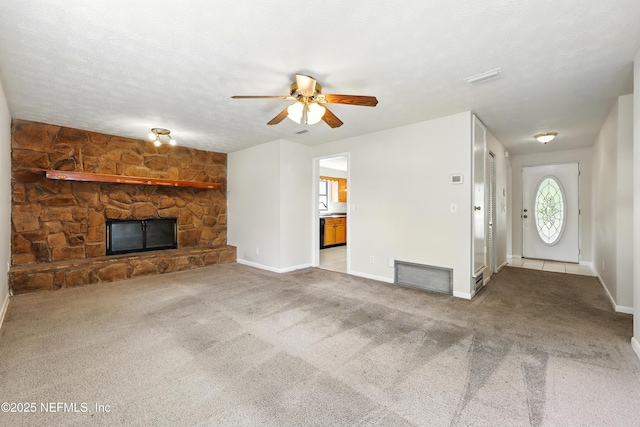 unfurnished living room with visible vents, baseboards, a stone fireplace, ceiling fan, and carpet