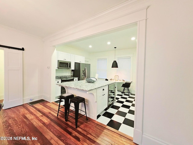 kitchen with a breakfast bar area, a barn door, baseboards, white cabinets, and stainless steel appliances