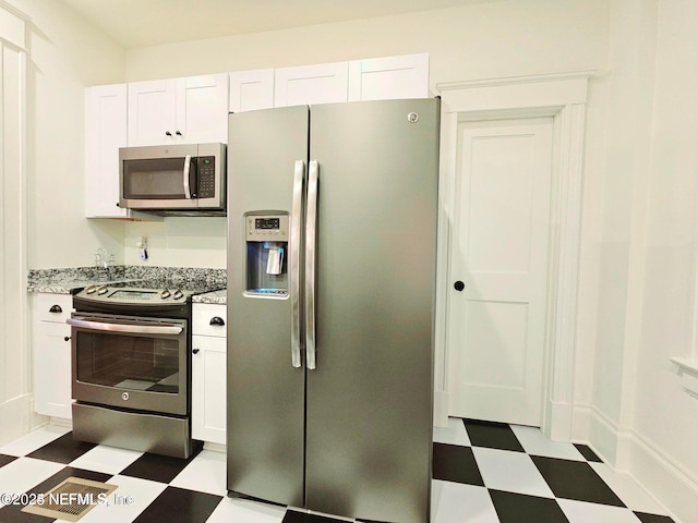 kitchen featuring light floors, light stone counters, stainless steel appliances, and white cabinetry